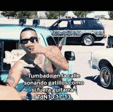 a man with a tattoo on his chest is standing in front of a car with the words tumbado en la calle sonando gatillos como