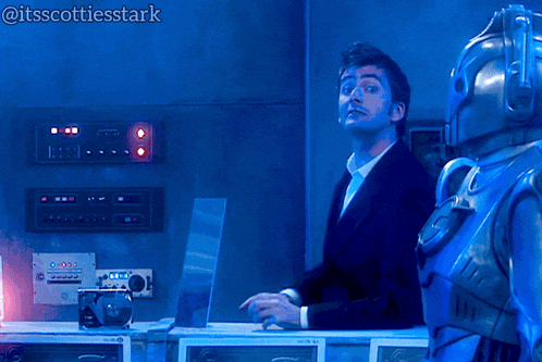 a man in a suit stands next to a robot in a blue room with the hashtag itsscottiesstark