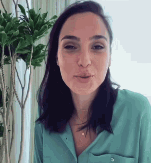 a woman wearing a blue shirt is standing in front of a plant