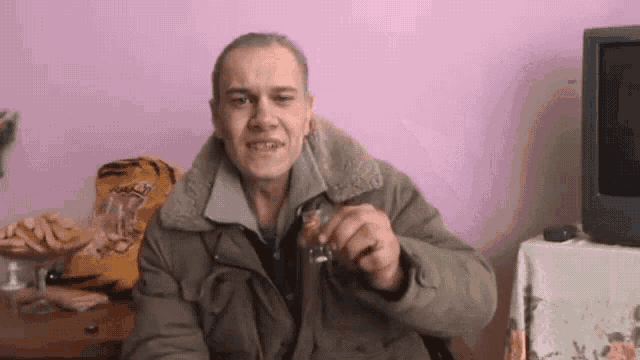 a man in a jacket is sitting in front of a tv holding a glass