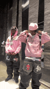 a man in a pink hoodie is standing next to another man in black jeans