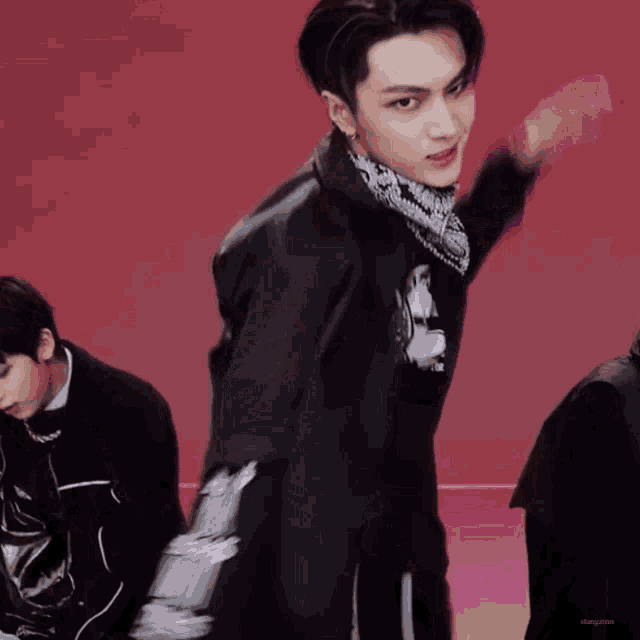 a man wearing a black jacket and a bandana is dancing in front of a red background