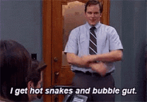 a man in a tie is standing in front of a group of people and says i get hot snakes and bubble gut