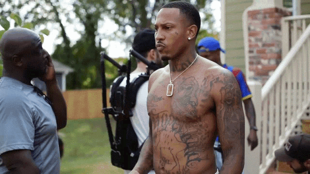 a man with a lot of tattoos on his chest is standing in front of a camera