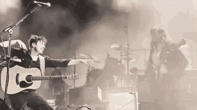 a man is playing a guitar and singing into a microphone while another man plays drums .