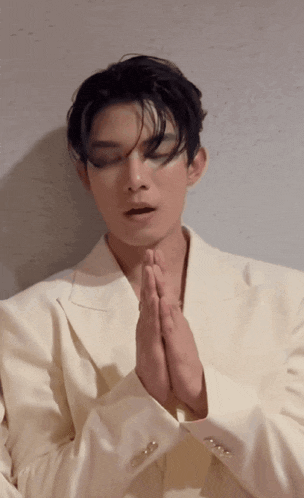 a man in a white suit is praying with his hands folded in front of his face