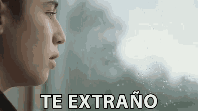 a man is looking out of a window with the words te extrano written in white letters .