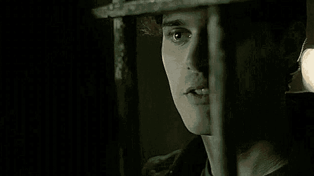 a close up of a man behind bars with his mouth open and a serious look on his face .