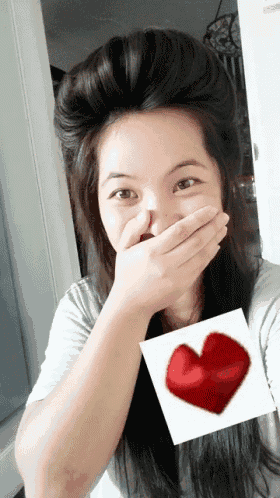 a woman covering her mouth with her hand and a red heart behind her