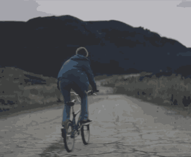 a boy in a blue jacket is riding a bike on a dirt road
