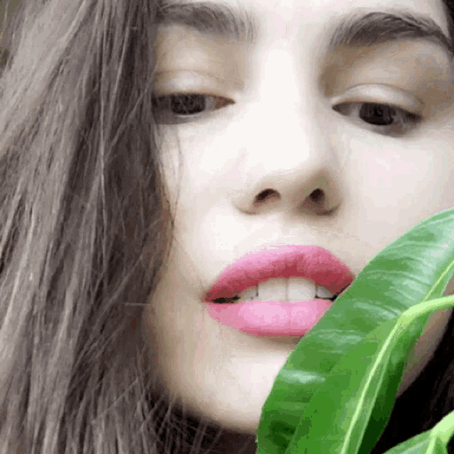 a close up of a woman 's face with pink lips and green leaves
