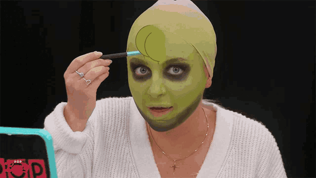 a woman with a green mask on her face is applying makeup in front of a mirror that says beauty pop
