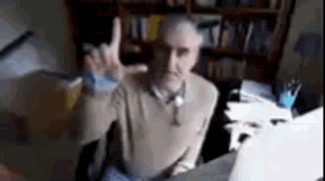 a man is sitting at a desk in front of a laptop computer and making a peace sign .