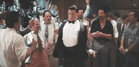 a man in a tuxedo is dancing in a crowd of people .