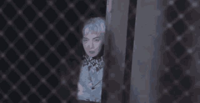 a man with white hair is behind a chain link fence and looking through it .