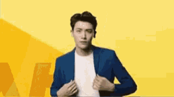 a man in a blue suit is standing in front of a yellow background and adjusting his jacket .