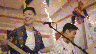 a man is playing a guitar and singing into a microphone while another man plays a guitar .
