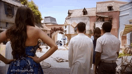 a woman in a blue dress is standing in front of a group of people looking at a city street .