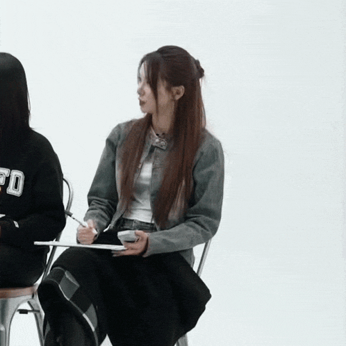 a girl wearing a sweatshirt that says fd sits in a chair with a notebook in her hand