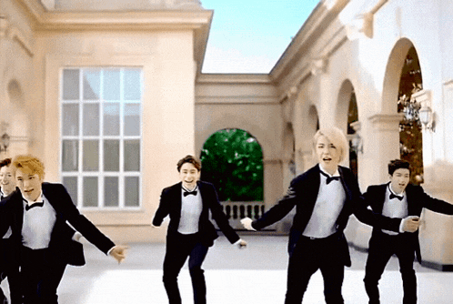 a group of young men in tuxedos and bow ties are dancing in front of a building