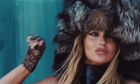 a woman wearing a fur hat and gloves is looking at the camera