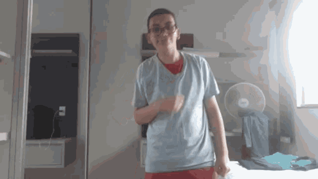 a man in a blue shirt is standing in a room with a fan