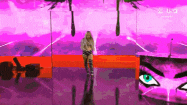 a woman is standing on a stage in front of a pink wall with a painting of a woman 's eye .
