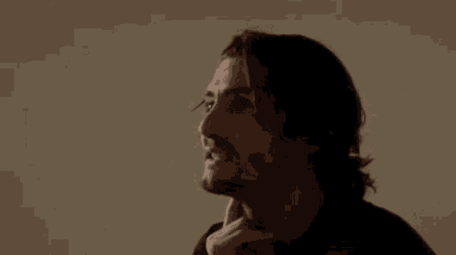 a man with long hair and a beard is holding his neck .