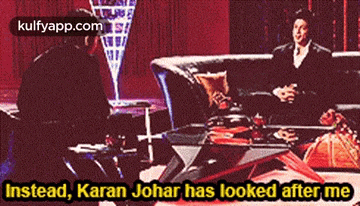 a man is sitting on a couch talking to another man with the words instead karan johar has looked after me .