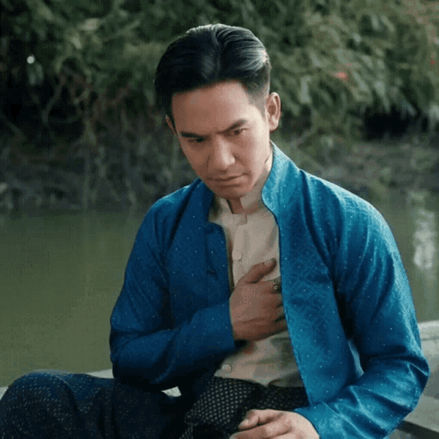 a man in a blue jacket is sitting on a dock with his hand on his chest
