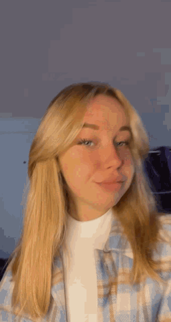 a girl with blonde hair is wearing a plaid shirt and a white shirt .