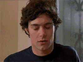 a man with curly hair is wearing a blue shirt and making a face .