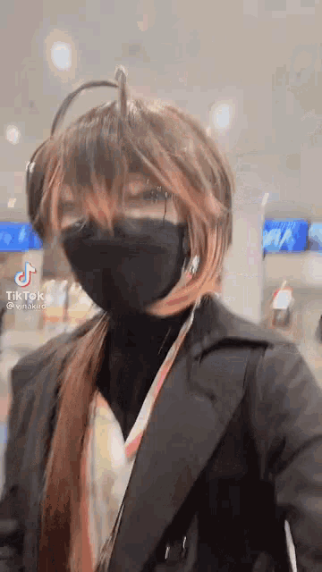 a woman wearing a black mask and a wig is standing in a room .