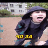 a young boy wearing a hooded jacket and a hat is standing in a park with his mouth open .