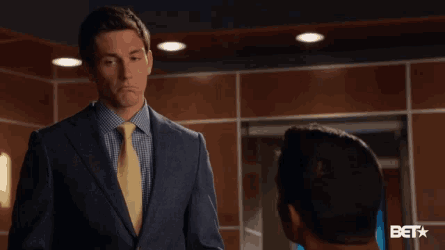 a man in a suit and tie is talking to another man in a room with a bet logo in the background
