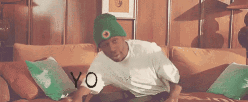 a man is sitting on a couch wearing a green beanie and a white shirt .