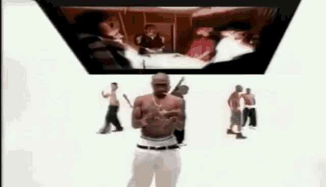 a man without a shirt is standing in front of a television screen surrounded by people .