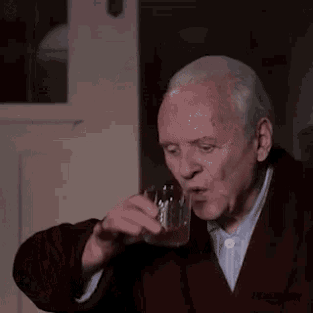a man in a suit is drinking from a glass in a dark room .