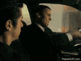 a man is sitting in the back seat of a car with another man in the front seat .