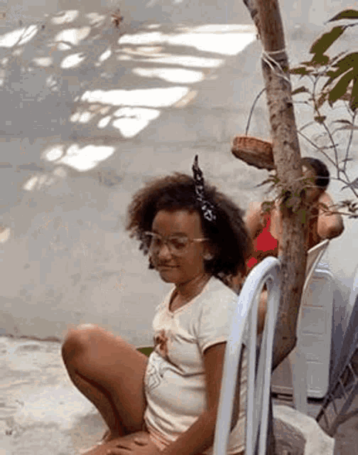 a little girl is sitting on the ground next to a tree .