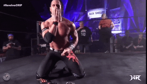 a wrestler is kneeling down in front of a sign that says alex shelley on it