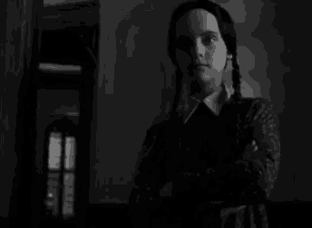 a black and white photo of a woman standing in a dark room looking at the camera .