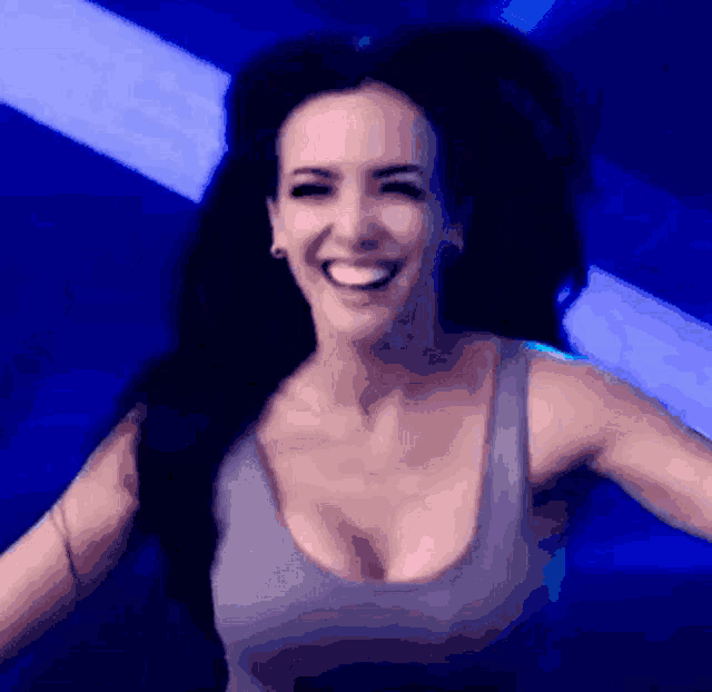 a woman in a gray tank top is smiling in front of a blue light .