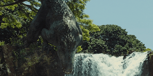 a statue of a dinosaur standing in front of a waterfall with trees in the background