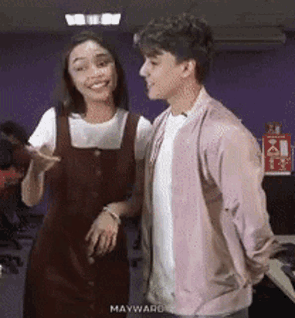 a man and a woman are standing next to each other and the man is wearing a pink cardigan .