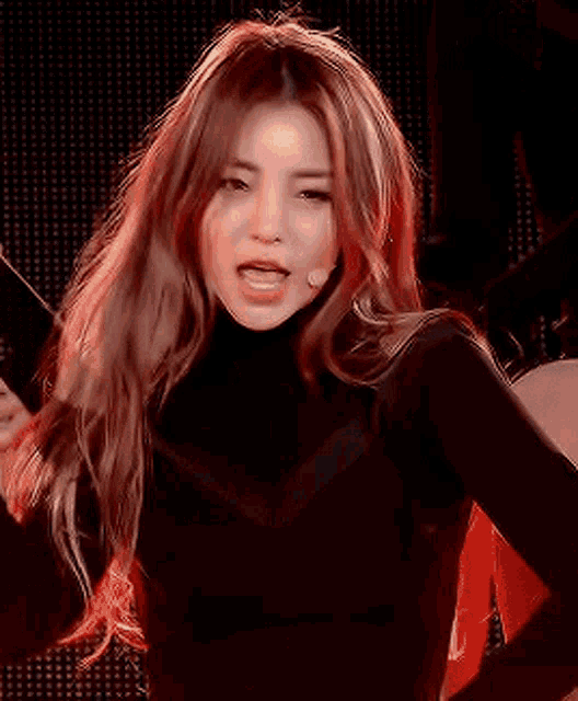a woman with long red hair is wearing a black turtleneck and a microphone in her mouth .