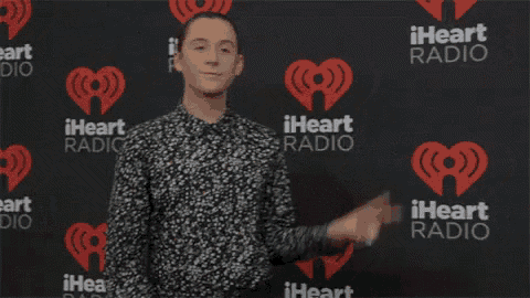 a man is giving a peace sign in front of a iheart radio wall .