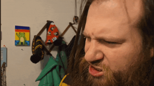 a man with a beard making a face in front of a frog painting