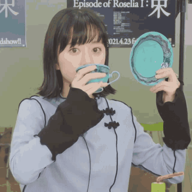 a girl is drinking from a blue cup in front of a poster that says episode of roselia