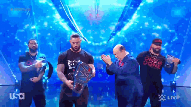 a man in a shirt that says greatness on a shirt holds a wrestling championship